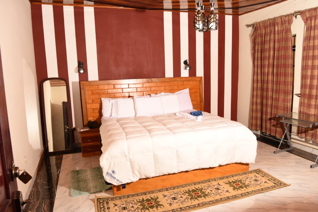 Chambre spacieuse avec grand lit en bois, tapis et murs rayés bordeaux